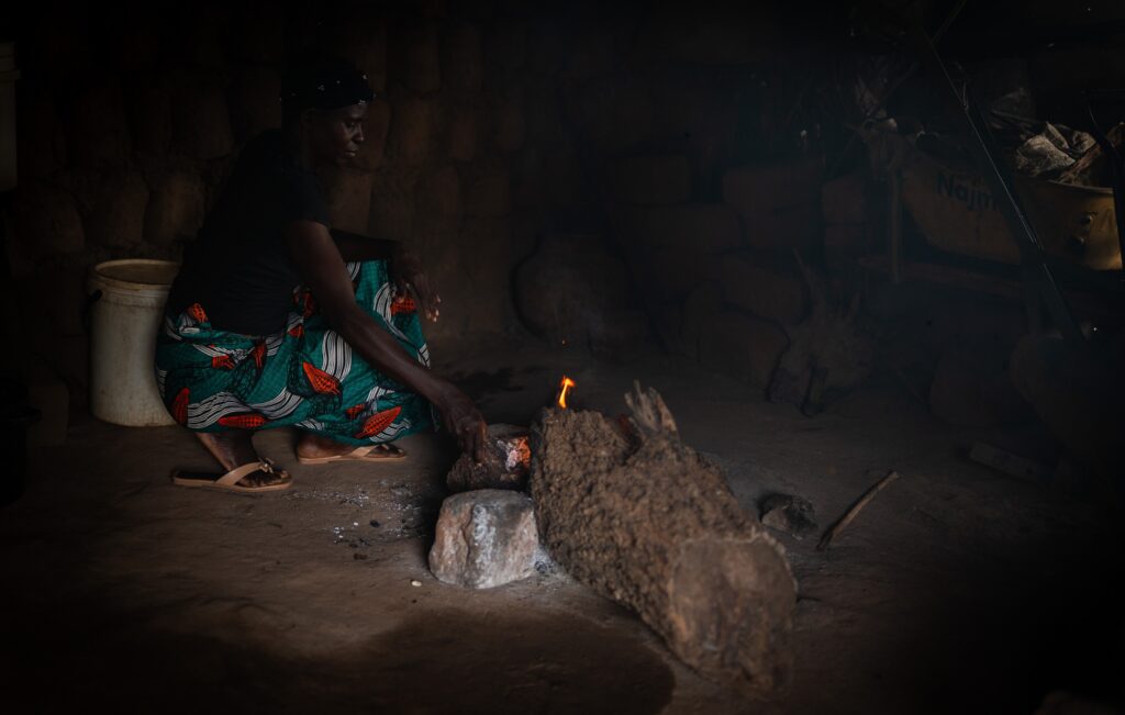 Fridah Luputa Mwale preparing a fire inside her home in low light after dark.
