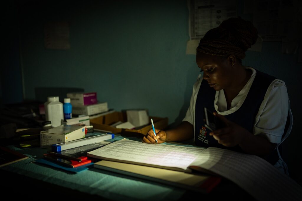 Cleopatra Maambo, a nurse at Ndubulula Health Post, using a torch as a source of light to write at the facility in Kantyatya Village.