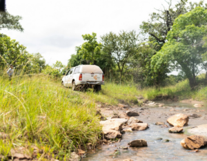 A SolarAid vehicle travels along a grassy track beside a stream.