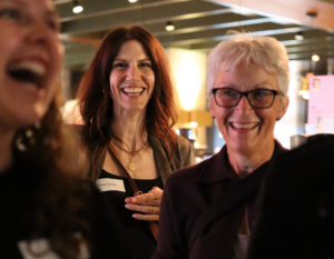 Two women smile at the camera during a SolarAid event, surrounded by other guests.