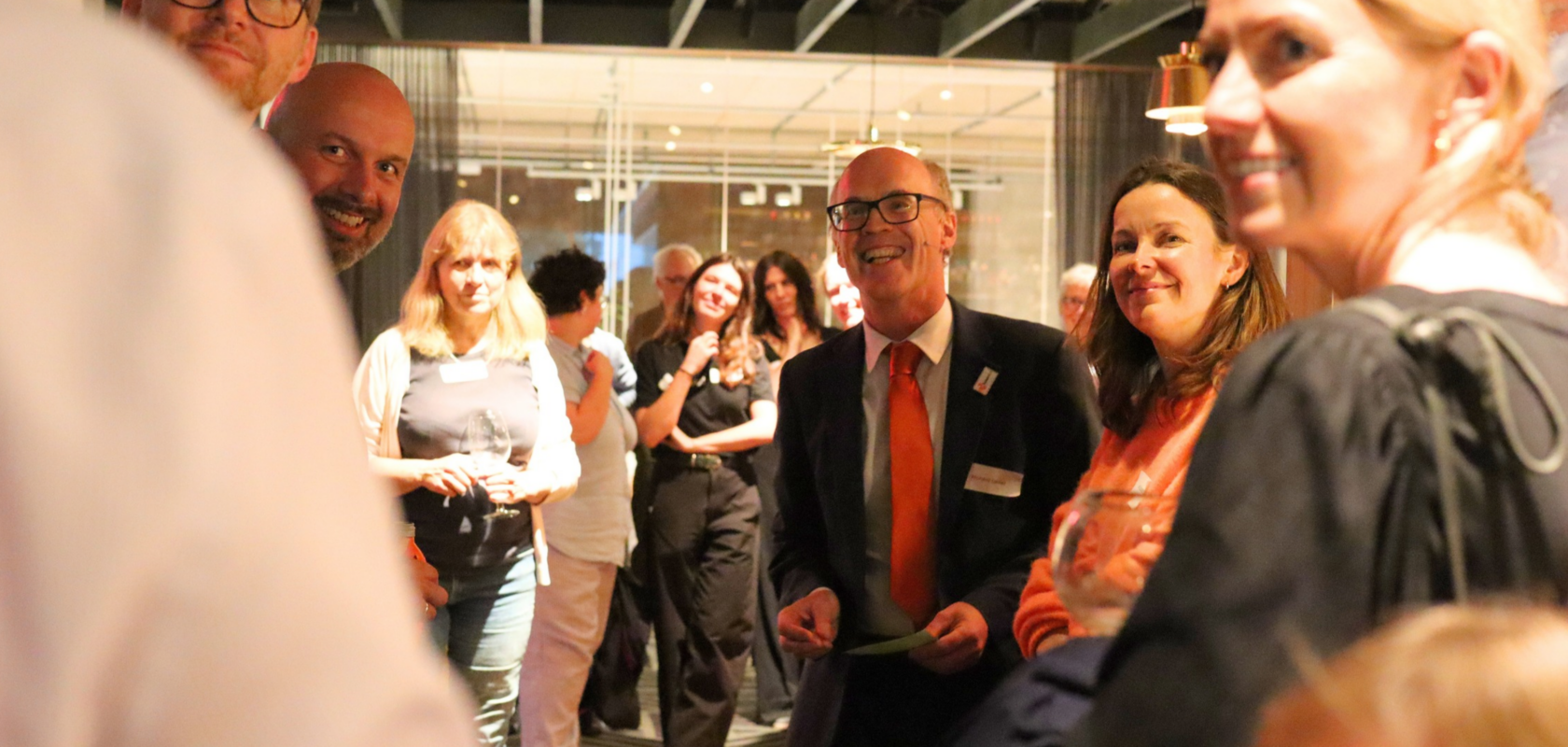 A group of SolarAid supporters chat and smile together at an event, with a man in a suit and red tie standing at the centre.