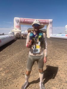 Man stands in front of the Marathon des Sables finish line.